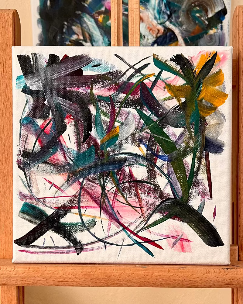 Abstract art on canvas displayed on a wooden easel against a beige wall.