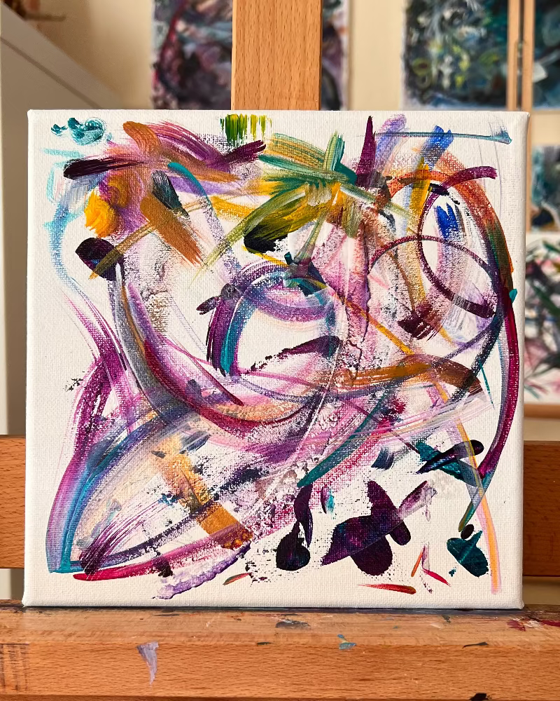 Abstract painting on a wooden easel with other artworks in the background