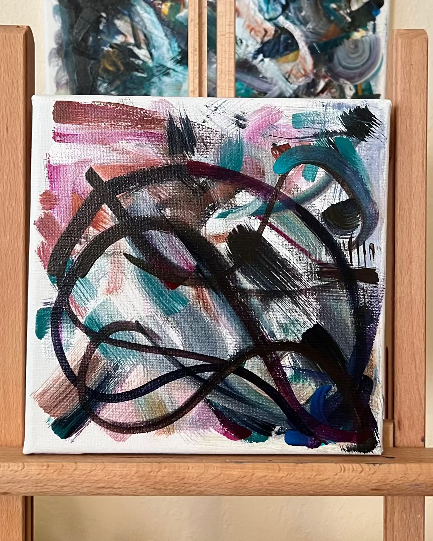 Abstract paintings on a wooden easel against a beige wall.