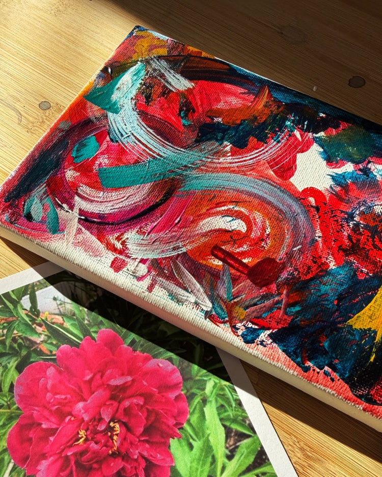 Colorful abstract painting on a wooden surface with a pink flower illustration below.