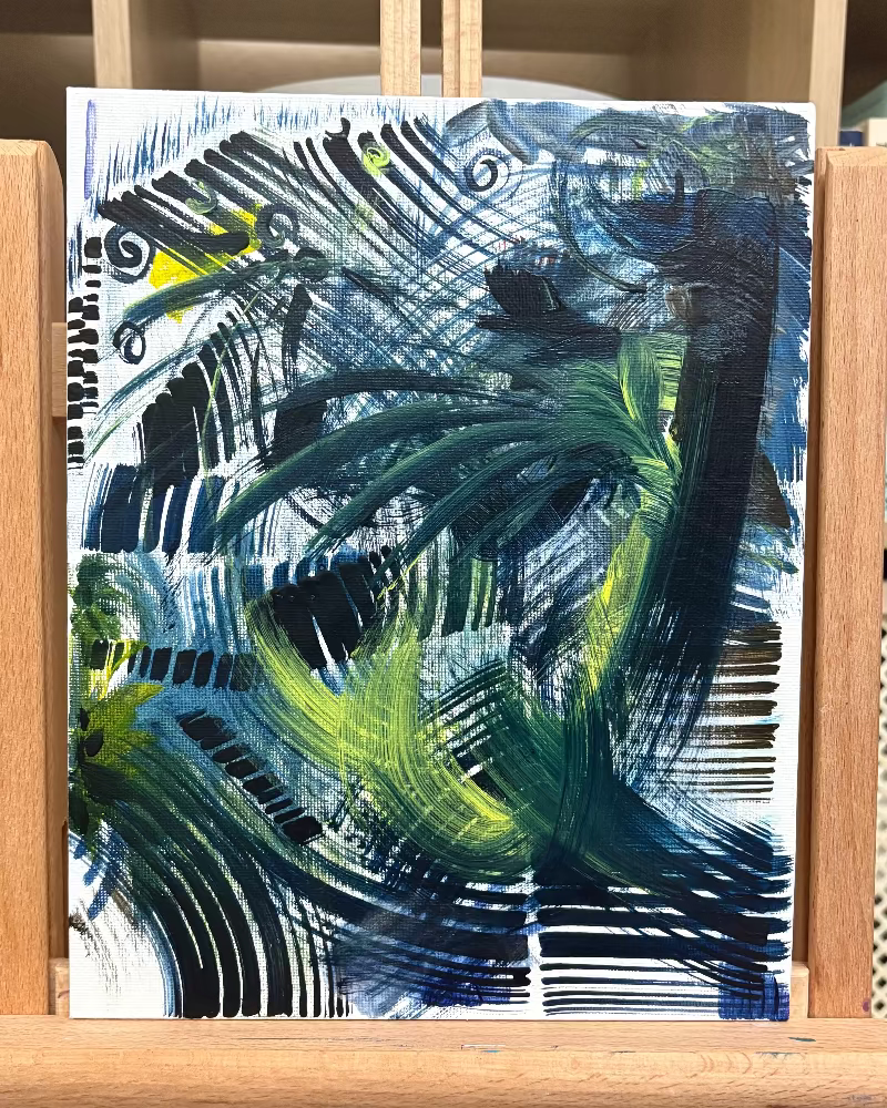 Abstract painting on a white background with black, green, and blue strokes, displayed on a wooden easel.