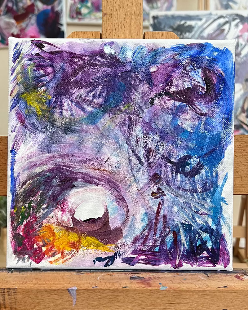 Abstract painting on a wooden easel with other artworks in the background