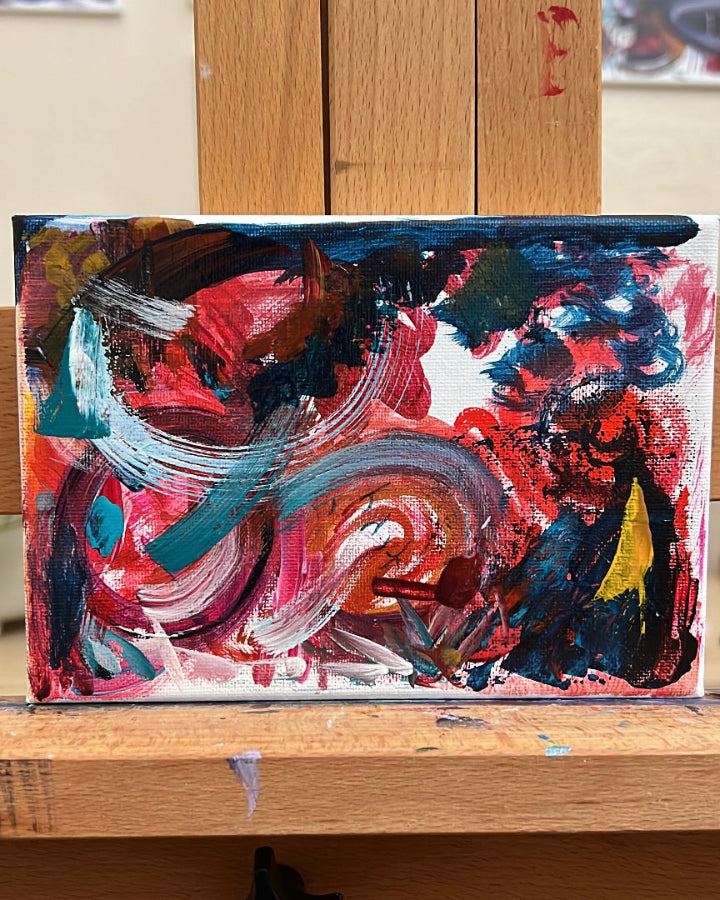 Colorful abstract painting on a wooden surface with a pink flower illustration below.